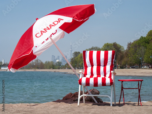 Photography A Canadian flag umbrella and red striped beach chair with the Toronto skyline in