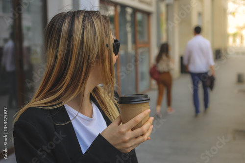 Portrait of young business woman walking on the street, in the morning with cup of coffee on her hand and wear sunglasses