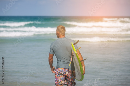 Photography Surfer boy in gray rash guard suit walking on the beach with surfboard to the oc
