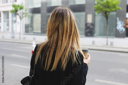 Portrait of young business woman walking on the street, in the morning with cup of coffee on her hand and wear sunglasses