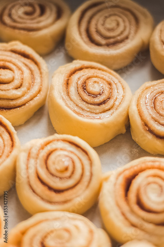 Delicious homemade raw cinnamon rolls bun dough in rectangle shaped baking tray on the white baking paper. Top view. Interesting pattern