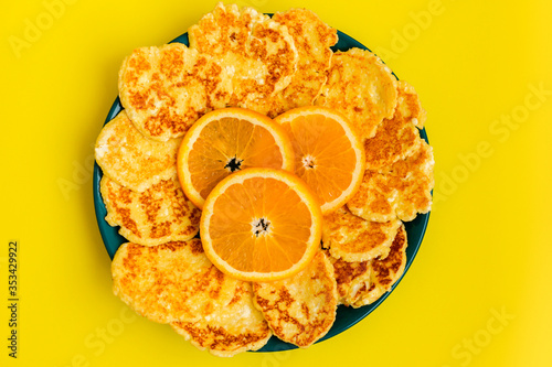Diet curd keto pancakes are in a green plate with orange slices on a yellow background.