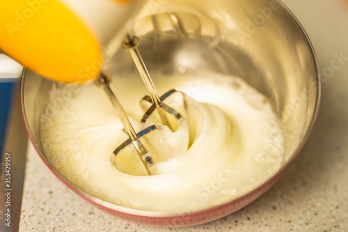 Beating a white cream with a mixer in a metal bowl. Whipped cream. Cream for the cake.