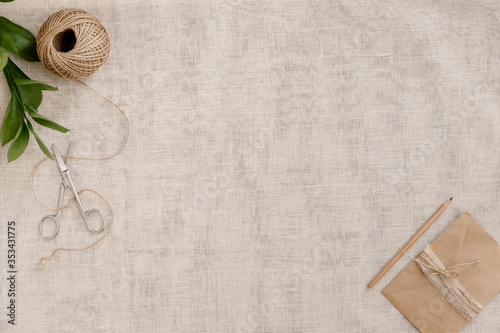 Top view image fashion designer background concept.Flat lay sewing scrapbooking accessory.Scissors, skein of twine, vintage envelope on brown linen fabric at home studio. Space for design mockup