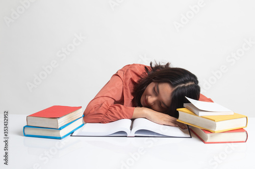 Exhausted Young Asian woman sleep with books on table .