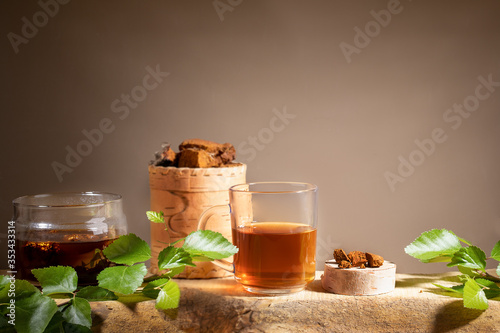 Healing beverage from birch mushroom chaga, chaga mushroom pieces, twigs on wooden plank on beige backdrop. Copy space. photo