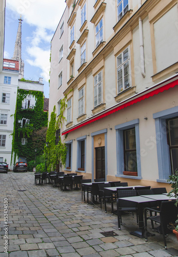 Small narrow street with tables and chairs, as touristic concept. Cityscape of narrow street with facade of building in city center of Vienna, Austria. 