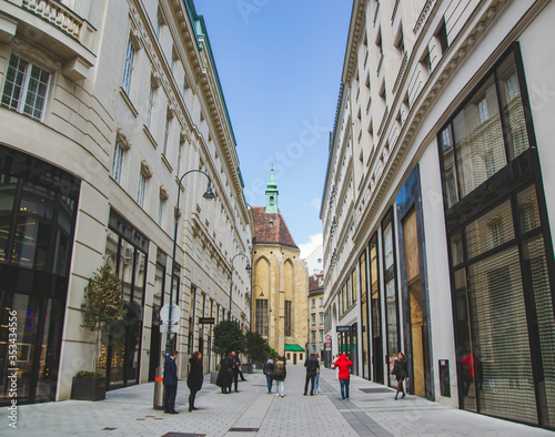 Urban cityscape of Vienna with church in the middle of the street. Touristic road with famous landmarks of downtown in the capital of Austria. Historical city center of city.