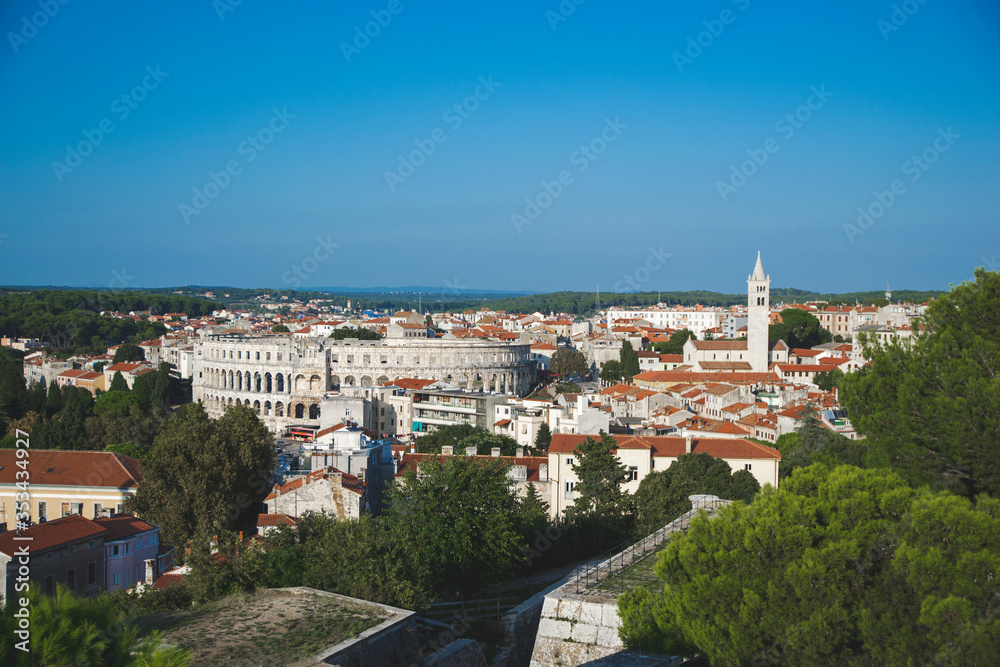 Landscape of Pula city, Croatia. Cityscape with orange rooftops, on the left side is staying colosseum and on the right side temple of church. Panorama view with big history. Tourism concept.