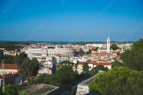 Landscape of Pula city, Croatia. Cityscape with orange rooftops, on the left side is staying colosseum and on the right side temple of church. Panorama view with big history. Tourism concept.