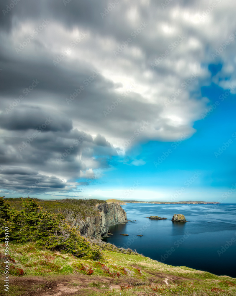 Pristine coastal seascape with soft clouds and sea stacks in beautiful clear blue water. Skerwink trail located in Port Rexton, Newfoundland Canada. Pristine coastal seascape with soft clouds and sea stacks in beautiful clear blue water. Skerwink trail located in Port Rexton, Newfoundland Canada.