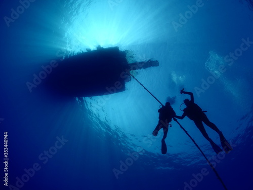 scuba divers ascending descending on the line of boat rope underwater blue decompression tank