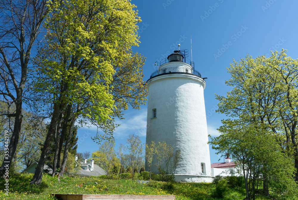 Suurupi upper lighthouse. Massive limestone building on the coast of Baltic sea. White tower between hardwood in spring. Blue sky and green foliage background. Interesting place to visit. Estonia.