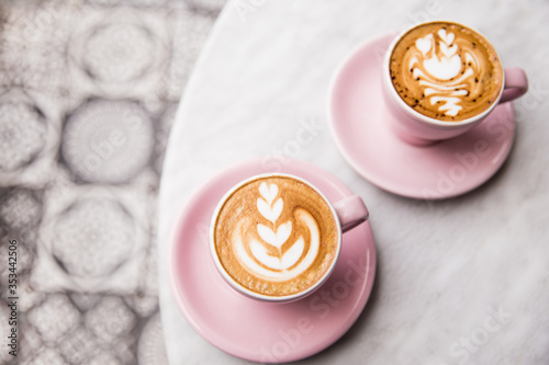 Two pink cups of cappuccino with beautiful latte art on marble table background.