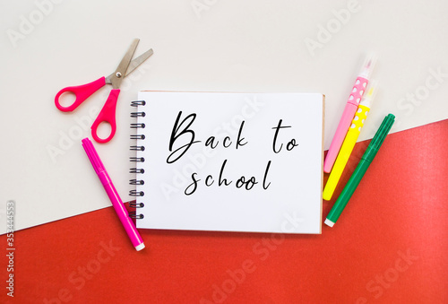 Colorful box with pencils, markers and scissors and a notebook on white and red background with copyspace. 2020 color trend. Back to school concept.