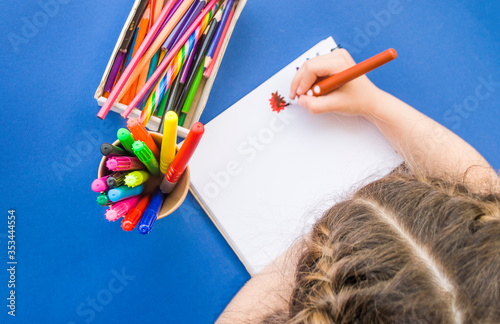 Child s drawing with colorful pencils and markers in a notebook on blue background with copyspace. Flat lay style. Back to school concept.