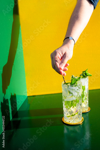 Mojito alcoholic cocktail with barman hand stirring ice on colorful background . New modern cockails drinks design concept photo