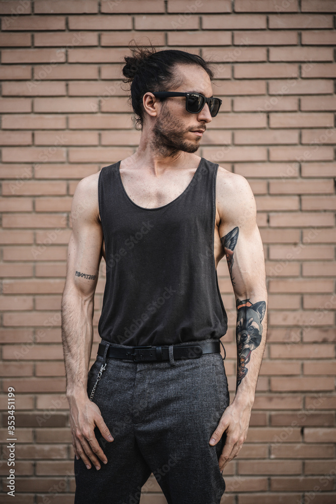 Modelo atlético con tatuajes posa con ropa y accesorios oscuros Modelo atlético con tatuajes posa con ropa y accesorios oscuros