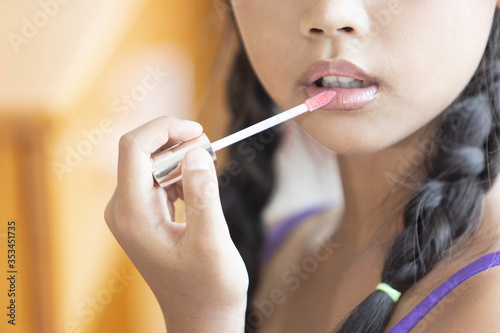 A cute long-haired Asian schoolgirl is using lipstick to apply lip makeup during a makeup lesson.