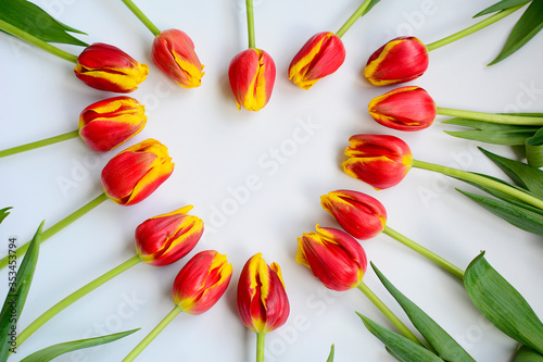 wers of red-yellow tulips lie in the shape of a heart on a white background. Festive composition. View from above.