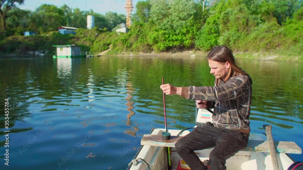 Narrow shot of fisherman with long hair setting fishing floater which is blue and has orange top. Man is very precise, thoughtful and careful. Narrow shot of fisherman with long hair setting fishing floater which is blue and has orange top. Man is very precise, thoughtful and careful.