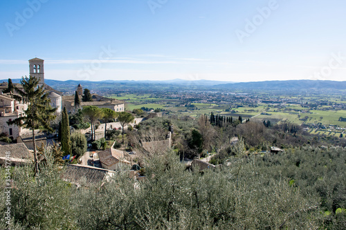 Pueblo medieval de Asís sobre las colinas en día soleado con valle verde de fondo photo