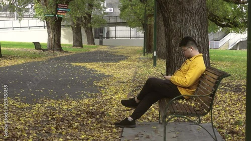Alone men with yellow jacket using smartphone in the park of the fall.
