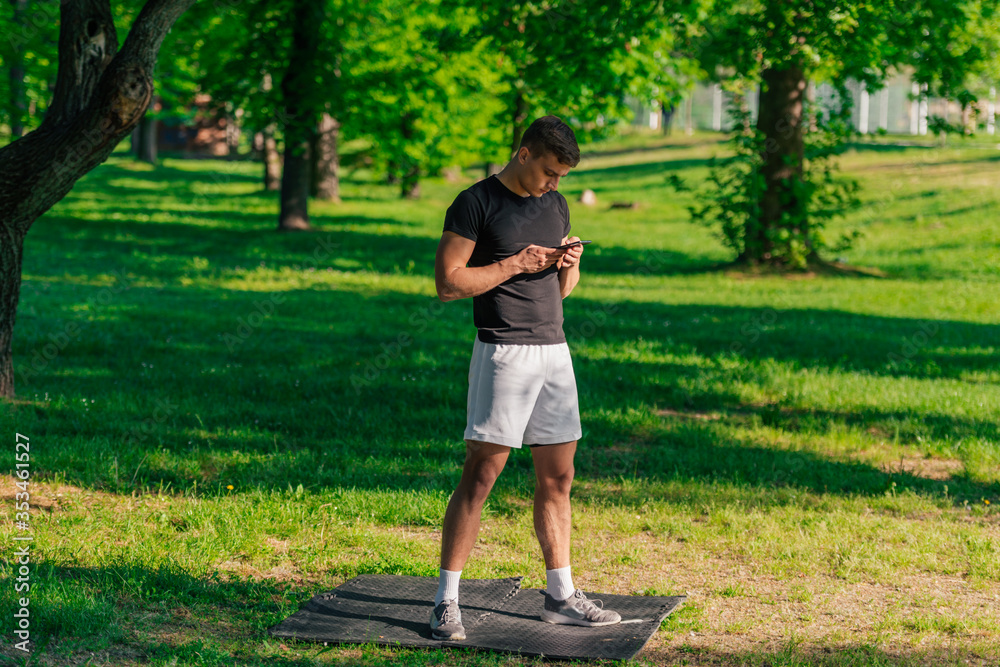 Athletic sportsman checking his phone while taking a break from a workout in the park Athletic sportsman checking his phone while taking a break from a workout in the park