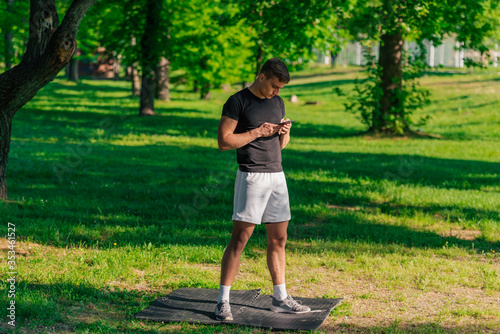 Athletic sportsman checking his phone while taking a break from a workout in the park