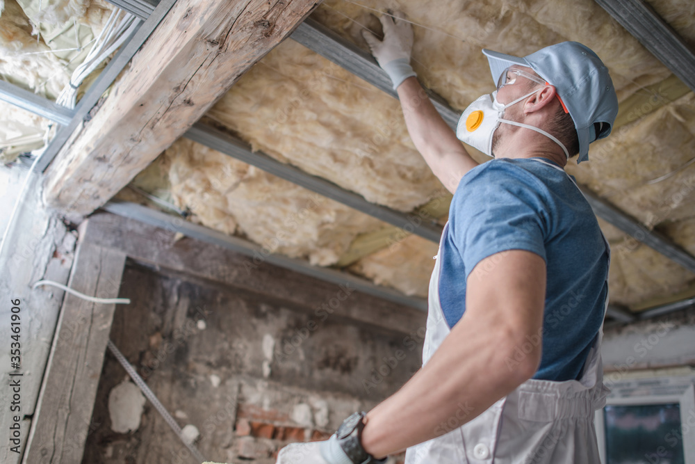 Caucasian Contractor Worker in His 30s Replacing Old Attic Mineral Wool Insulation. Wearing Safe Breath Pro Mask. Industrial Home Improvement and Insulation Materials Theme. Caucasian Contractor Worker in His 30s Replacing Old Attic Mineral Wool Insulation. Wearing Safe Breath Pro Mask. Industrial Home Improvement and Insulation Materials Theme.