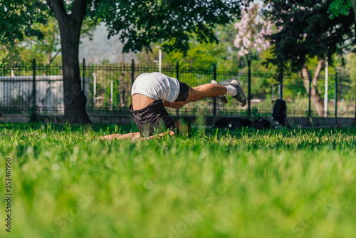 Young sporty handsome man practicing yoga in the park and doing the plow pose..