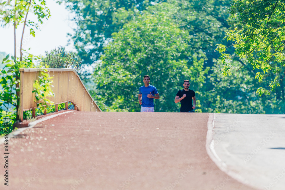 Two young male friends are running through the forest on a jogging trail. Two young male friends are running through the forest on a jogging trail.