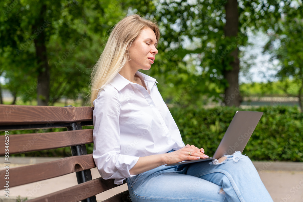 young woman working online through a laptop while sitting on a bench in a country park