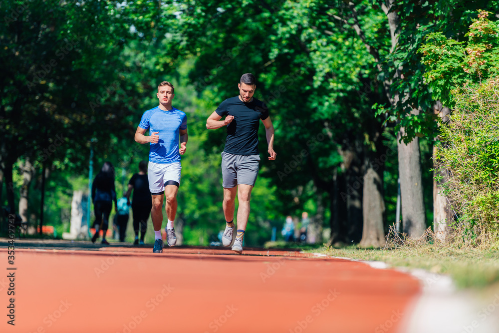 Two healthy young men running in the park on a sunny day.. Two healthy young men running in the park on a sunny day..