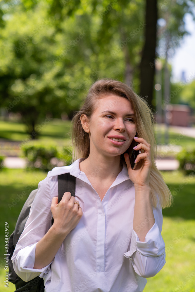young woman of European appearance walking in the park and smiling talking on the phone young woman of European appearance walking in the park and smiling talking on the phone