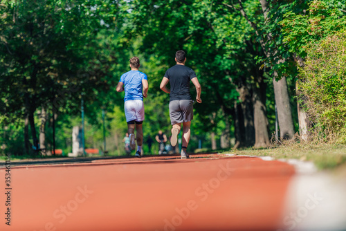 Rearview of two male friends running outdoors in a park © qunica.com