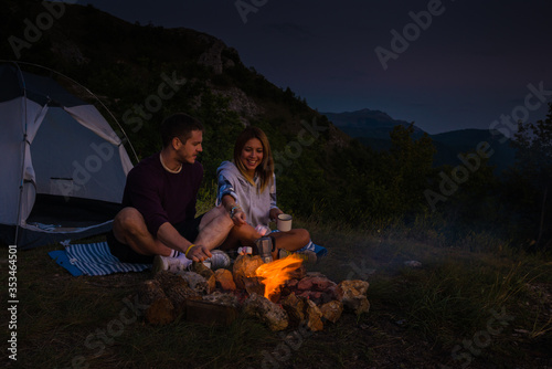 Young couple relaxing by the campfire and drinking coffee in the forest hill in the dusk photo