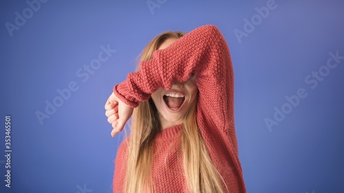 BeautifuBeautiful blond girl laughing out loud and covering her eyes with the hand. Isolated on blue background.  photo