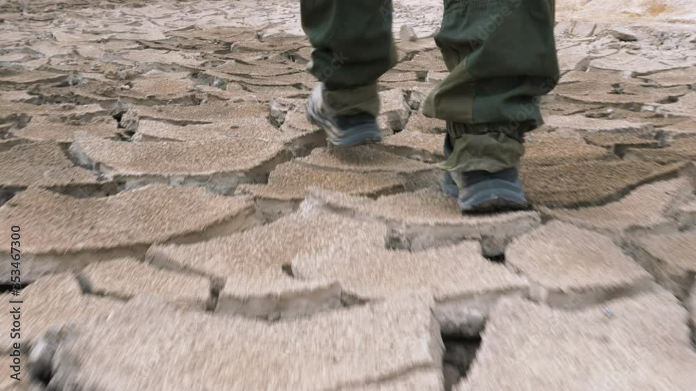 A man in boots walks on cracked earth during a drought and environmental disaster. The concept of environmental pollution and post apocalypse A man in boots walks on cracked earth during a drought and environmental disaster. The concept of environmental pollution and post apocalypse