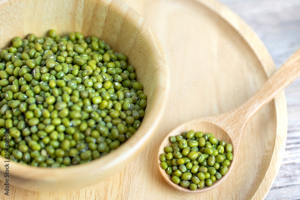 Raw fresh mung beans seed or organic green beans in a wooden bowl and wooden spoon isolated on the wooden plate table background.Healthy food ,Agriculture concept.Copy space. Raw fresh mung beans seed or organic green beans in a wooden bowl and wooden spoon isolated on the wooden plate table background.Healthy food ,Agriculture concept.Copy space.