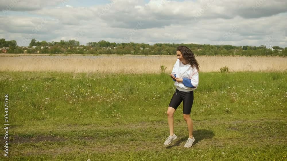 Beautiful cheerful girl of Caucasian appearance walks in the park looks at the phone and listens to music on headphones Beautiful cheerful girl of Caucasian appearance walks in the park looks at the phone and listens to music on headphones