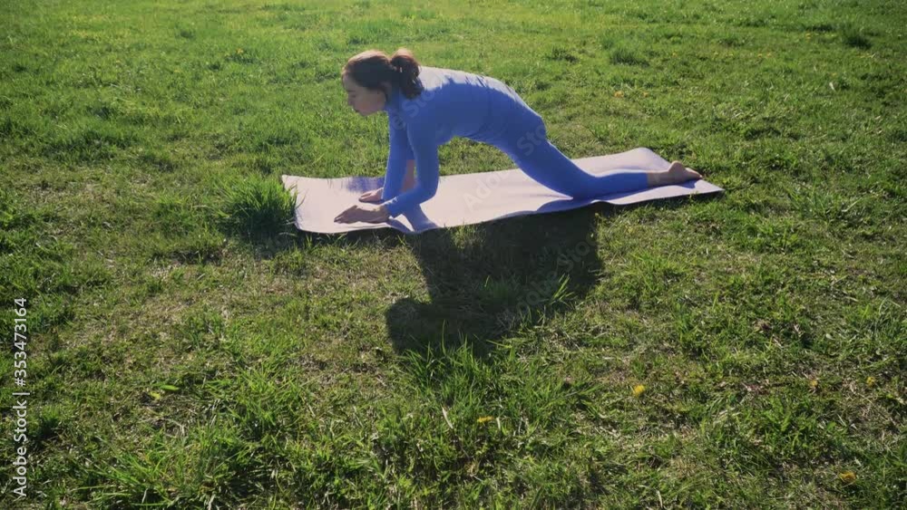 A young girl in a tracksuit is standing on a rug in a park doing yoga. The concept of meditation in the fresh air on a sunny day at sunset. A young girl in a tracksuit is standing on a rug in a park doing yoga. The concept of meditation in the fresh air on a sunny day at sunset.