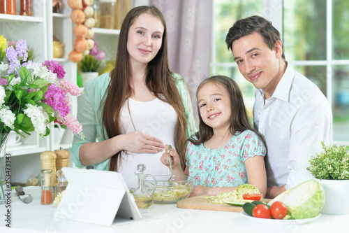 Happy pregnant woman with husband and daughter preparing salad together