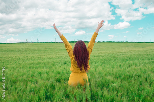  Young happy woman with luxurious hair raised her hands up in a wheat field against the sky. Harvesting a rich harvest