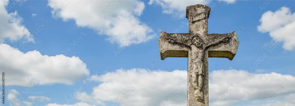 Beautiful very old and ancient statue of the crucifixion of Jesus Christ against blue sky with clouds. Free copy space.