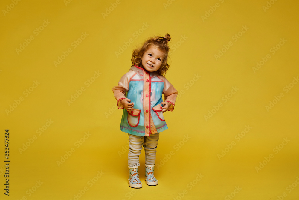 Cute little girl in a modish raincoat and rubber boots isolated at the yellow background. Child fashion. Copy space Cute little girl in a modish raincoat and rubber boots isolated at the yellow background. Child fashion. Copy space
