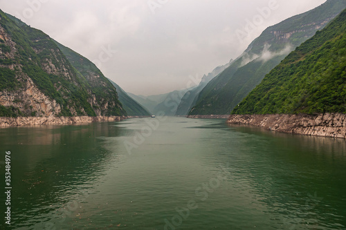 Wushan, Hubei, China - May 7, 2010: Wu Gorge in Yangtze River. Shoreline split forms steep short canyon between green covered mountain walls under silver sky behind green water.