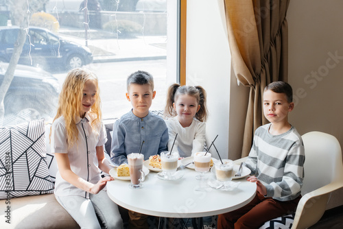 A large friendly company of children celebrate the holiday in a cafe with a delicious dessert. The day of the birth © Andrii