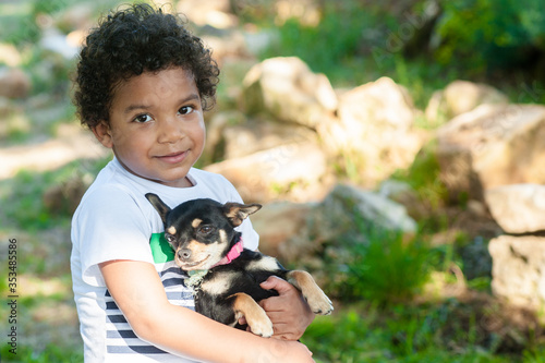 African young boy holding his little dog in nature.