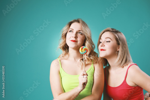 Two twins women holding colorful  lollipops and  having fun in studio isolated on green background .